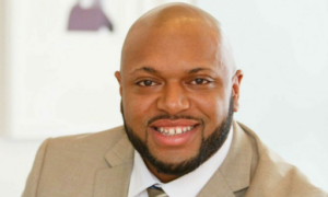 Andre smiles in tan suit for a headshot.